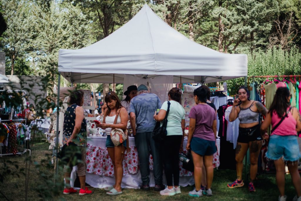 A small business tent at a farmer's market with many customers surrounding it.