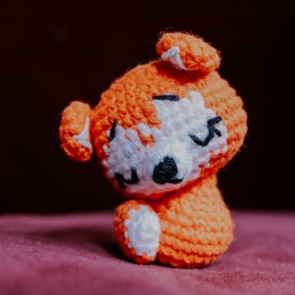 A crocheted orange and white fox with its head tilted to the side.
